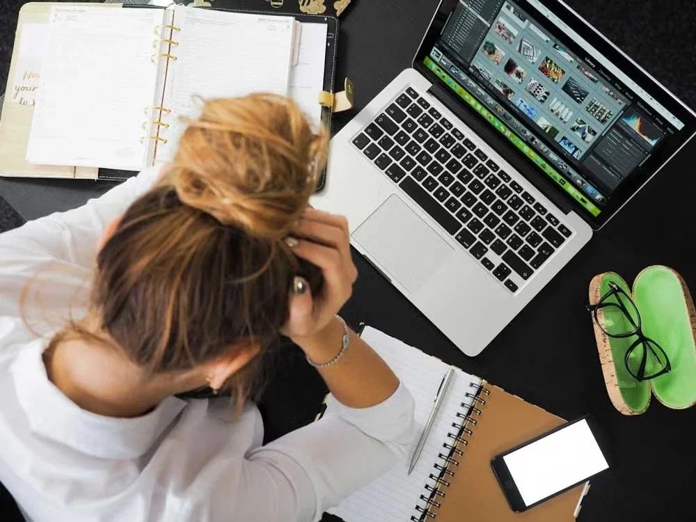 Overhead view of a person stressed at a desk with a laptop, planner, glasses, and smartphone.