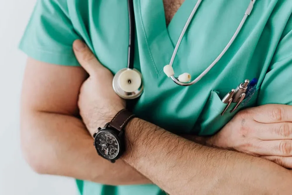 Close-up of a healthcare worker in green scrubs with stethoscope and wristwatch.