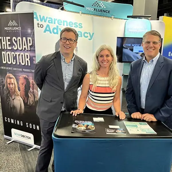 Three individuals at a promotional booth with informational banners and brochures.