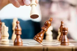 A hand moving a white queen chess piece on a chessboard.