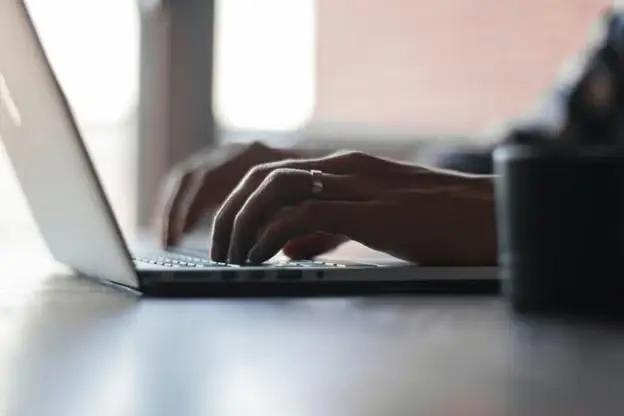 Close-up of hands typing on a laptop keyboard with a blurred background.