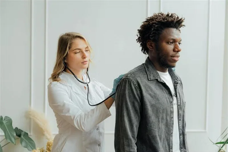 Doctor in white coat using a stethoscope on a patient's back.