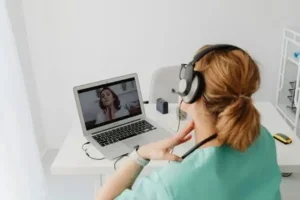 A person with headphones sitting at a desk with a laptop, involved in a video call.